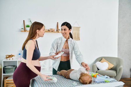 Photo for A young beautiful mother lovingly stands next to her baby on a bed, receiving guidance from her coach at parents courses. - Royalty Free Image