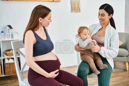 Une femme enceinte assise, berçant un bébé dans ses bras, symbolisant l'amour, l'éducation et le voyage de la maternité.
