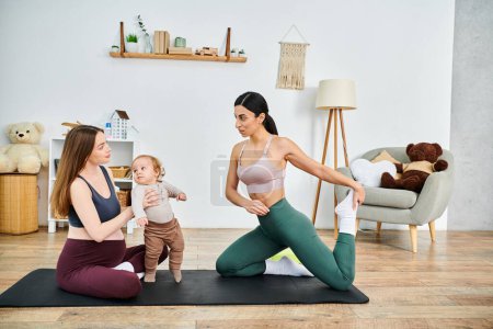 Foto de Una joven y hermosa madre está sentada en una esterilla de yoga, sosteniendo suavemente a su bebé mientras recibe orientación de su entrenador. - Imagen libre de derechos