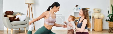 Eine schöne junge Mutter in Sport-BH und Leggings tanzt fröhlich mit einem Kleinkind zu Hause, angeleitet von ihrem Trainer aus Elternkursen.
