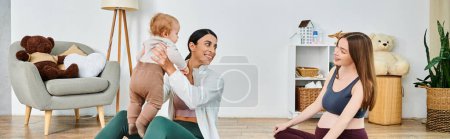 Téléchargez les photos : Une jeune, belle mère assise sur le sol, berçant son bébé avec soin, tout en recevant des conseils d'un entraîneur lors de cours de parents. - en image libre de droit