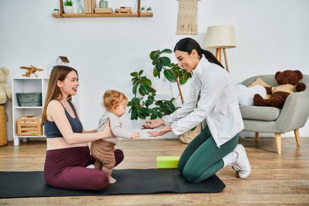 Téléchargez les photos : Une jeune belle mère et son bébé s'engagent dans une séance de yoga paisible guidée par leur instructeur lors d'un cours de parents. - en image libre de droit