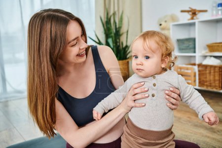 Eine junge, schöne Mutter wiegt ihr Baby auf dem Arm und lässt sich bei Elternkursen von ihrem Trainer beraten.