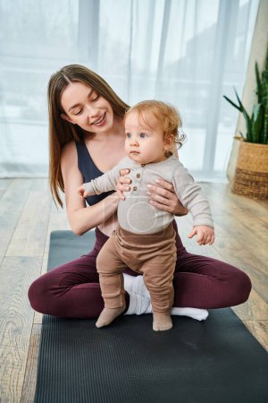 Una joven madre sostiene suavemente a su bebé en una esterilla de yoga, guiada por un entrenador en los cursos de los padres en la comodidad de su hogar.