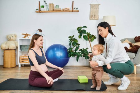 A young, beautiful mother peacefully holds her baby on a yoga mat at home, guided by her coach from parent courses.