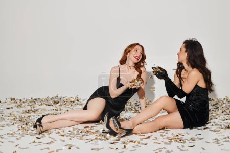 Foto de Dos mujeres elegantes, una pareja lesbiana cariñosa, se sientan en una cama de confeti, irradiando alegría y paz. - Imagen libre de derechos