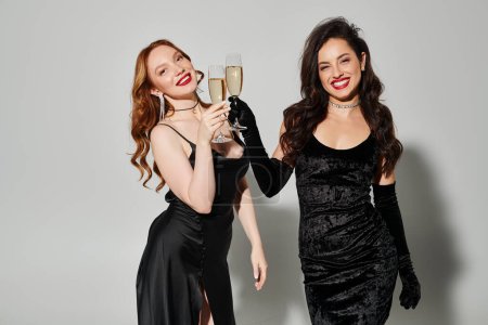 Two women in black dresses celebrating with champagne flutes.