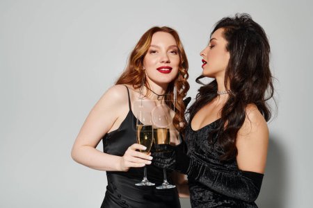 Two happy women in black dresses enjoying wine together.