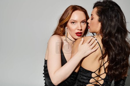 Two women in black dresses embrace and share a loving kiss.
