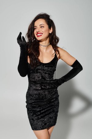Una mujer con un vestido negro y guantes posando elegantemente en un ambiente elegante.