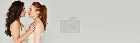 Photo for A loving lesbian couple in elegant attires pose happily next to each other in front of a white wall. - Royalty Free Image