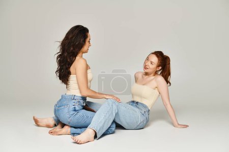 Téléchargez les photos : Deux femmes élégamment habillées s'assoient sur le sol, absorbées par une conversation profonde. - en image libre de droit