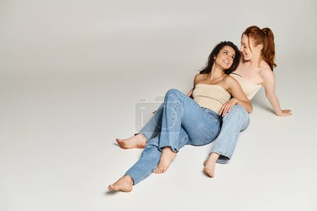 Foto de Dos mujeres elegantes, una pareja lesbiana cariñosa, se sientan en el suelo juntos. - Imagen libre de derechos