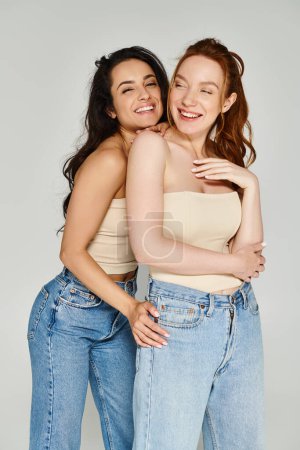 Dos mujeres jóvenes con elegante atuendo se abrazan firmemente, radiantes de felicidad.