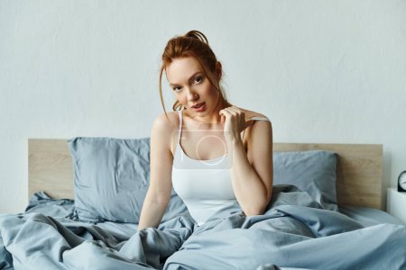 Una mujer en traje elegante se sienta en una cama con sábanas azules, exudando calma.