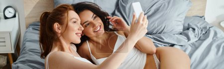 Téléchargez les photos : Deux femmes joyeuses, élégamment vêtues, blotties sur un lit dans une étreinte aimante. - en image libre de droit
