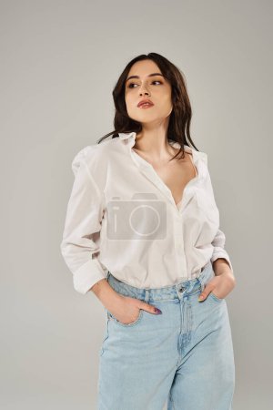 A beautiful, plus size woman posing gracefully in stylish white shirt and jeans against a gray backdrop.