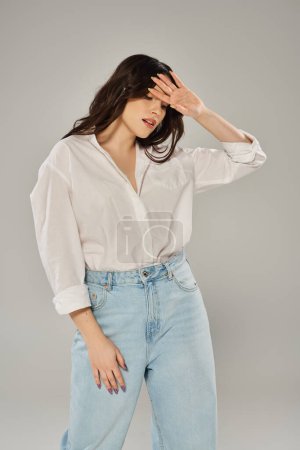 A beautiful plus-sized woman striking a pose in a white shirt and jeans, exuding confidence and style against a gray backdrop.