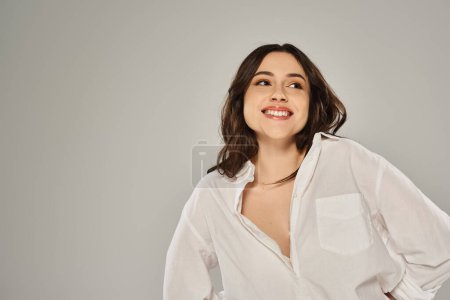Stylish plus size woman in white shirt striking a pose against a gray backdrop.