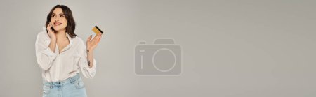 Téléchargez les photos : A beautiful plus-size woman in stylish attire holds a cell phone against a gray backdrop. - en image libre de droit
