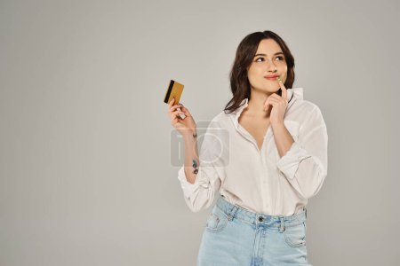 Plus size woman in white shirt exudes elegance while holding a gold card against a gray backdrop.