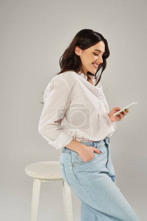 Une femme de taille plus en tenue élégante s'assoit sur un tabouret, absorbée dans son téléphone portable.