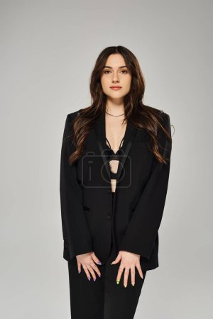 Photo for A beautiful plus-size woman in a black suit strikes a confident pose against a gray backdrop. - Royalty Free Image