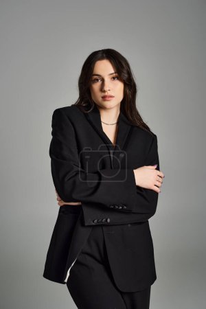 Stylische Plus-Size-Frau rockt einen schwarzen Anzug, der vor neutralem Hintergrund Zuversicht und Anmut ausstrahlt.