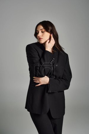 A beautiful plus size woman strikes a pose in a sleek black suit on a gray backdrop.