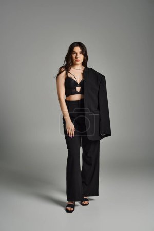 Eine atemberaubende Plus-Size-Frau posiert in einem eleganten schwarzen Oberteil und einer Hose vor grauem Hintergrund.