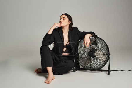 Plus size woman in stylish attire sitting gracefully next to a fan, embracing a moment of peace and serenity.