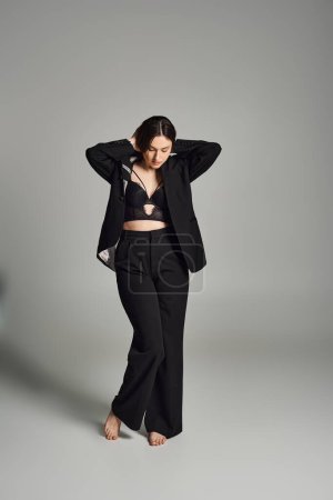 A beautiful plus size woman exudes confidence in a striking black suit, striking a pose against a gray backdrop.