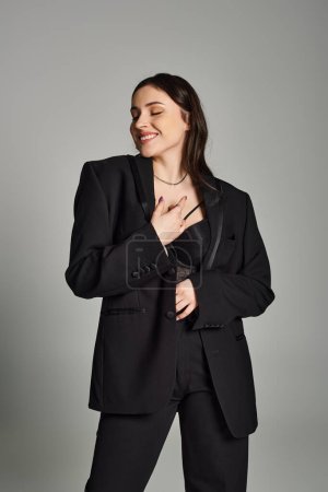 A stunning plus size woman in a black suit confidently posing for the camera against a gray backdrop.