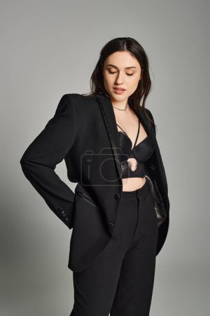 Photo for A stunning plus size woman in a sleek black suit strikes a confident pose against a gray backdrop. - Royalty Free Image