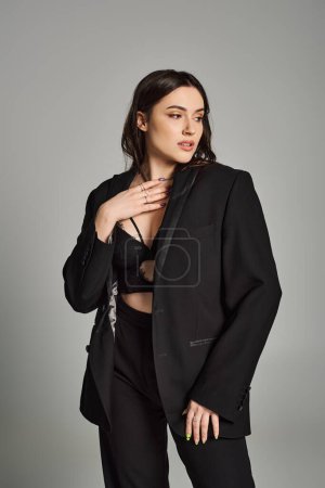 A beautiful plus size woman in a black suit striking a confident pose against a gray backdrop.