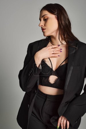 Téléchargez les photos : A stunning plus size woman confidently poses in a black suit and bra against a gray backdrop. - en image libre de droit