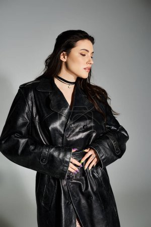 Photo for A stunning plus size woman poses confidently in a chic black leather coat on a gray backdrop. - Royalty Free Image