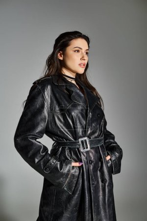 Stylish plus size woman in a black coat poses gracefully on a gray backdrop.