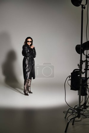 Photo for A plus-size woman in stylish attire confidently poses in a studio setting, with a camera capturing her grace and beauty. - Royalty Free Image