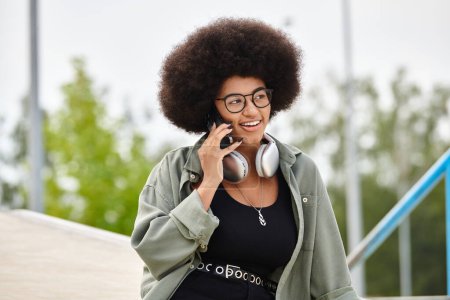 A stylish woman with an afro hairstyle chats on her smartphone while enjoying the outdoors.