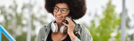 Una mujer elegante con el pelo rizado y gafas habla en su teléfono celular en un entorno al aire libre.