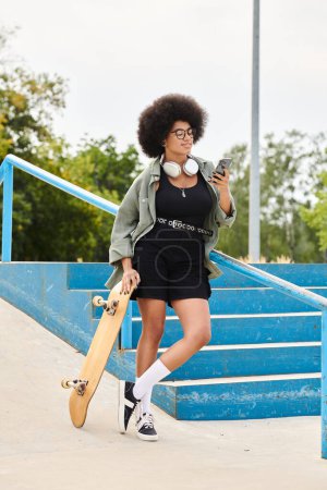 Eine junge Afroamerikanerin mit lockigem Haar hält ein Skateboard und ein Handy im Freien in einem Skatepark.