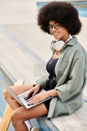 Eine junge Frau mit lockigem Haar entspannt sich auf einer Bank, vertieft in ihren Laptop in einem lebhaften Skatepark.