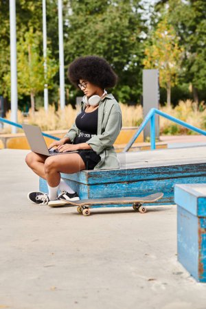 Eine junge Afroamerikanerin mit lockigem Haar sitzt draußen auf einer Bank und arbeitet intensiv an ihrem Laptop..