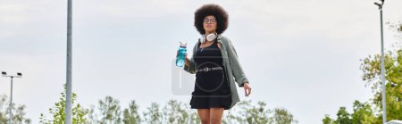 Young African American woman with a curly afro hair riding a skateboard at a skate park.