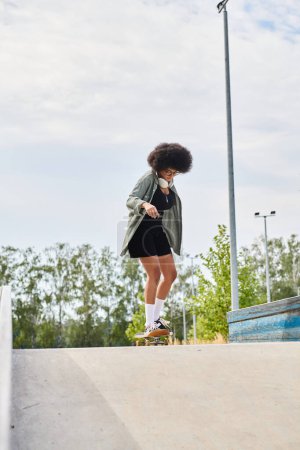 A young African American woman with curly hair confidently rides a skateboard down a cement ramp at an outdoor skate park.