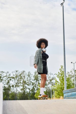 A young African American woman with curly hair skillfully balances on a skateboard at the top of a ramp in a vibrant skate park setting.