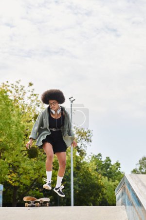 Photo for A young African American woman with curly hair jumps her skateboard high in the air at an outdoor skate park. - Royalty Free Image