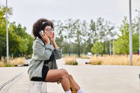 Una mujer con el pelo rizado usando auriculares mientras está sentada en un banco al aire libre en una ciudad bulliciosa.