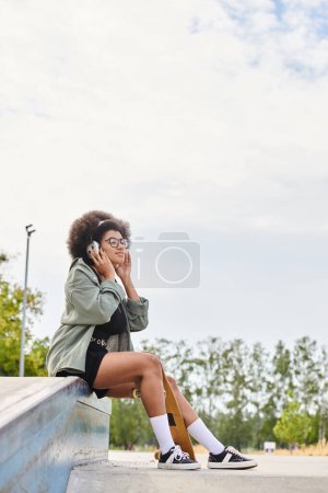 A young African American woman with curly hair, sitting on a ledge, engaged in a phone conversation in an urban setting.